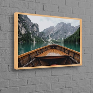 May include: A wooden boat on a calm lake with a view of mountains in the background. The boat is facing the viewer and the water is a deep blue color.