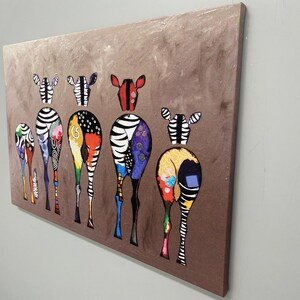 May include: A colorful painting of seven zebras with their backs to the viewer. The zebras are painted in a variety of colors, including black, white, red, yellow, blue, green, and purple. The zebras are standing in a line, and the background is a brown color.