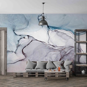 May include: A contemporary living room with an abstract mural in blue, white, and grey. The room includes a pallet sofa with grey cushions, a wooden door, a metal and wood shelving unit, and an industrial-style pendant light.