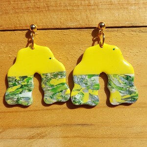 Könnte beinhalten: Ein Paar gelbe und grüne Statement-Ohrringe mit Marmorierung. Die Ohrringe sind bogenförmig und haben einen goldenen Haken.