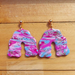 Könnte beinhalten: Ein Paar abstrakte Ohrringe in Pink, Blau und Silber mit goldenen Haken.