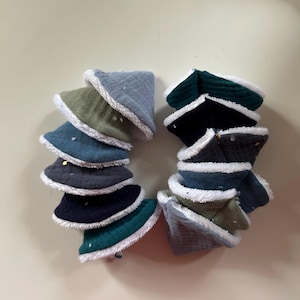 May include: A collection of small, soft bucket hats in various colors, including teal, navy, olive green, and gray. Each hat features a white, fluffy trim around the brim. Some hats have small gold embellishments.