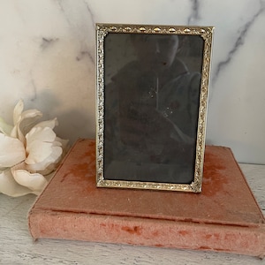 May include: A silver picture frame with an ornate design sits on a pink velvet book. The frame is empty and ready for a photo.