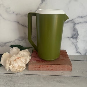 May include: A green plastic pitcher with a white lid. The pitcher is sitting on a book.