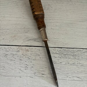 May include: A vintage screwdriver with a wooden handle and a metal shaft. The handle has a dark brown finish and is slightly worn. The shaft is made of metal and has a silver finish.