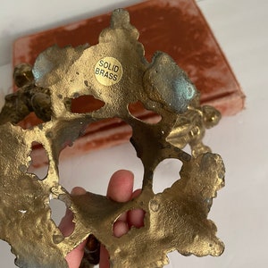 May include: The underside of a solid brass decorative object with an ornate design. The object has a label that reads "SOLID BRASS".