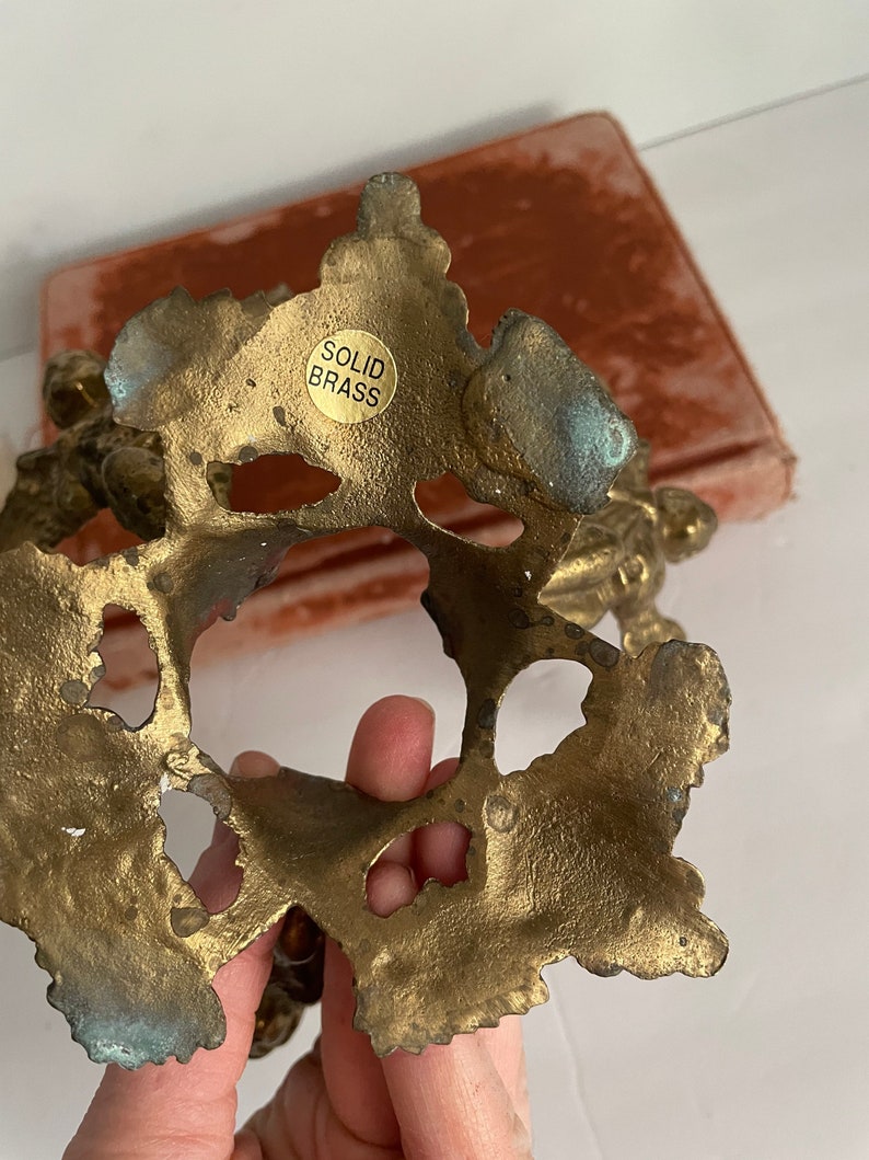 May include: The underside of a solid brass decorative object with an ornate design. The object has a label that reads "SOLID BRASS".