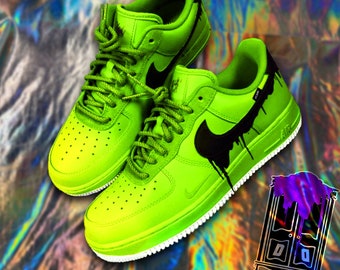 May include: A pair of neon green sneakers with black Nike swoosh logos and black paint dripping down the sides. The sneakers have white soles.