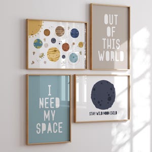 May include: Four framed prints with a space theme. The top left print features a yellow sun and planets with faces. The top right print has a beige background with the text "OUT OF THIS WORLD". The bottom left print has a light blue background with the text "I NEED MY SPACE". The bottom right print has a white background with a dark blue moon and the text "STAY WILD MOON CHILD".
