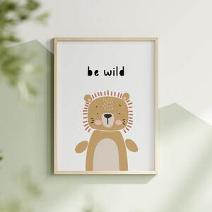 K&ouml;nnte beinhalten: Ein gerahmter Kunstdruck mit einer Cartoon-L&ouml;wen-Illustration in Braun-, Beige- und Pfirsicht&ouml;nen. Der Text "be wild" ist &uuml;ber dem L&ouml;wen aufgedruckt. Das Kunstwerk ist vor einem wei&szlig;en Hintergrund und in einem hellen Holzrahmen gerahmt.