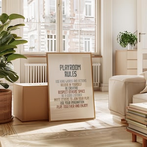Op de afbeelding: Een ingelijst print met de tekst "Speelkamerregels" en een lijst met regels voor een speelkamer, waaronder "Gebruik vriendelijke woorden en daden", "Geloof in jezelf", "Wees creatief", "Respecteer de ruimte van anderen", "Wees een goede luisteraar", "Nodig anderen uit om mee te spelen", "Gebruik je verbeelding" en "Speel samen en geniet!"