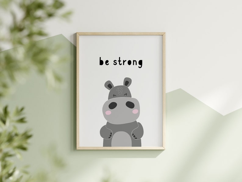 K&ouml;nnte beinhalten: Gerahmter Kunstdruck mit einer Cartoon-Nilpferd-Illustration in Graut&ouml;nen, mit rosa Akzenten und einem freundlichen Ausdruck. Die Worte "be strong" sind in Schwarz &uuml;ber dem Nilpferd gedruckt. Das Kunstwerk befindet sich vor einem wei&szlig;en Hintergrund.