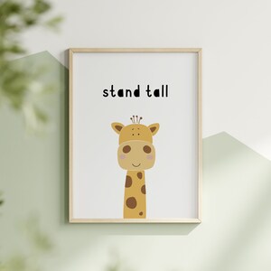 K&ouml;nnte beinhalten: Gerahmter Druck mit einer Cartoon-Giraffen-Illustration. Die Giraffe ist beige mit braunen Flecken und einem hellbraunen Kopf. Die Worte "stand tall" stehen in Schwarz &uuml;ber der Giraffe. Der Rahmen ist hellbraun.