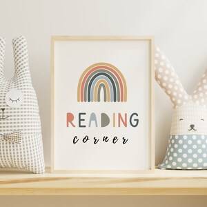 May include: A framed print featuring a rainbow design and the text "READING corner" in black lettering. Two plush bunny toys are on a wooden shelf either side of the print.