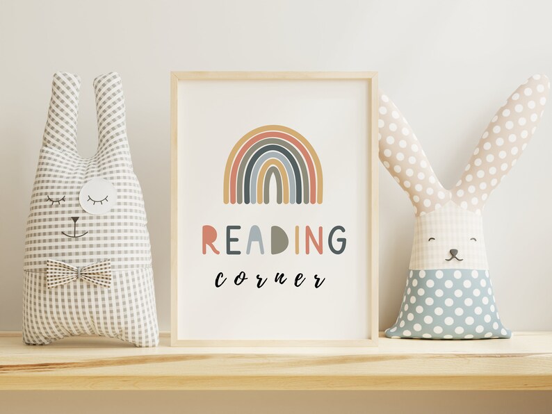 May include: A framed print featuring a rainbow design and the text "READING corner" in black lettering. Two plush bunny toys are on a wooden shelf either side of the print.