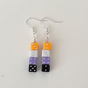 May include: Dangle earrings with a non-binary pride flag design. Each earring has four stacked square beads in yellow, white, purple, and black, with silver-coloured ear wires. The beads have white dots.