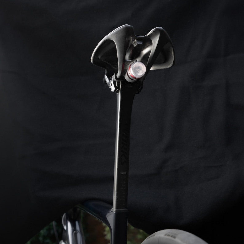 May include: Black bicycle seat post with a black and red bicycle light attached to the top.