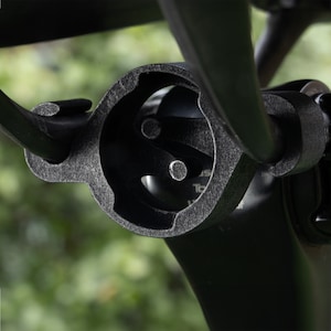 Puede incluir: Primer plano de un soporte de manillar de bicicleta negro con una superficie texturizada. El soporte tiene una abertura circular con un dise&ntilde;o de tres puntas en el interior.