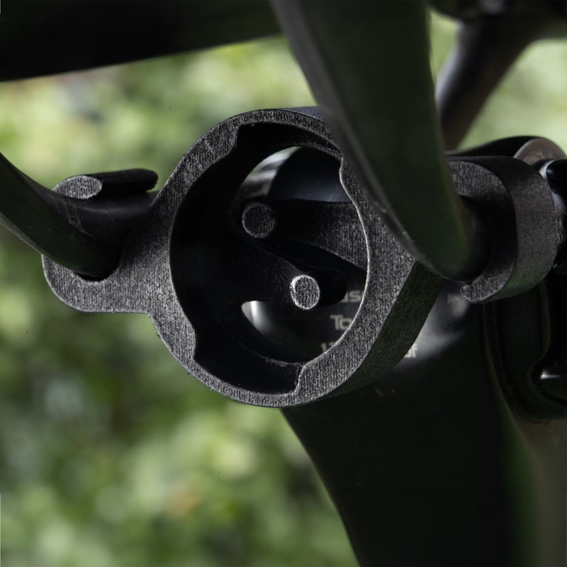 Puede incluir: Primer plano de un soporte de manillar de bicicleta negro con una superficie texturizada. El soporte tiene una abertura circular con un dise&ntilde;o de tres puntas en el interior.