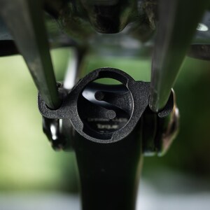 Puede incluir: Primer plano de una tija de sill&iacute;n de bicicleta negra con un soporte redondo de pl&aacute;stico negro para una c&aacute;mara o luz. El soporte tiene una abertura circular con un peque&ntilde;o c&iacute;rculo elevado en el centro.