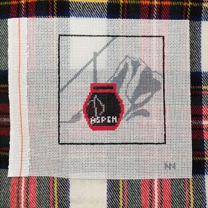 May include: A white canvas with a black frame, featuring a black and red design of a ski lift with the word "Aspen" on the bottom.
