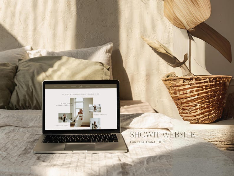 K&ouml;nnte beinhalten: Ein Laptop-Computer, auf dem eine Website f&uuml;r Fotografen angezeigt wird. Die Website hei&szlig;t "Showit" und hat einen hellen Hintergrund mit Bildern von Personen in verschiedenen Posen. Der Laptop steht auf einem wei&szlig;en Bettlaken mit einem Weidenkorb und einer Pflanze im Hintergrund.