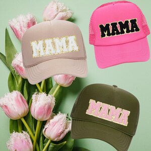 May include: Three trucker hats with the word "MAMA" in gold glitter letters on the front. The hats are in pink, beige, and olive green.
