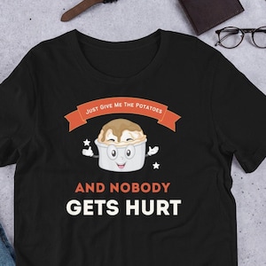 Op de afbeelding: Zwart T-shirt met een witte cartoonillustratie van een pot met aardappelen met oogjes en de tekst "Just give me the potatoes and nobody gets hurt."