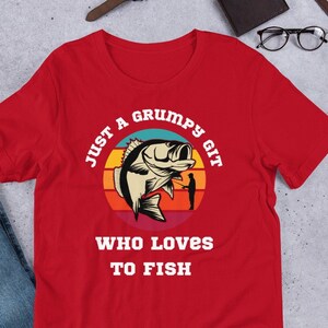 Może przedstawiać: Czerwona koszulka z grafiką w stylu vintage ryby i tekstem "Just a grumpy git who loves to fish".
