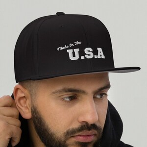 Puede incluir: Una gorra de béisbol negra ajustada con un logotipo bordado en blanco que dice "Made in the U.S.A."