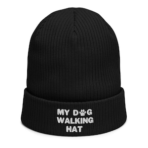 Könnte beinhalten: Schwarze Strickmütze mit einer weißen gestickten Pfote und dem Text "MY DOG WALKING HAT".