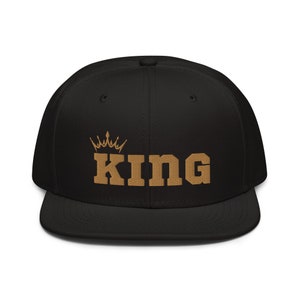 May include: Black and gold embroidered baseball cap with the word "KING" and a crown above it.
