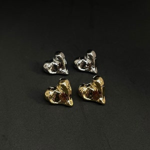 Könnte beinhalten: Vier herzförmige Ohrringe, zwei silber und zwei gold. Die Ohrringe sind alle leicht unregelmäßig geformt, was ihnen einen einzigartigen und modernen Look verleiht.