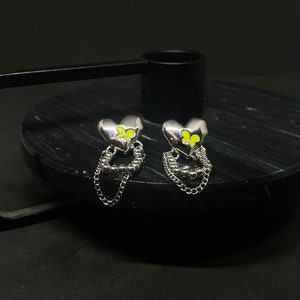 Könnte beinhalten: Ein Paar silberne herzförmige Ohrringe mit einer baumelnden Kette und gelben Schmetterlingsakzenten.