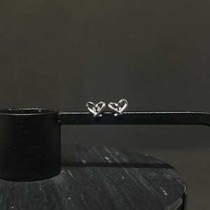 May include: A pair of silver heart-shaped stud earrings. The earrings are made of a single piece of wire that is twisted into a heart shape.