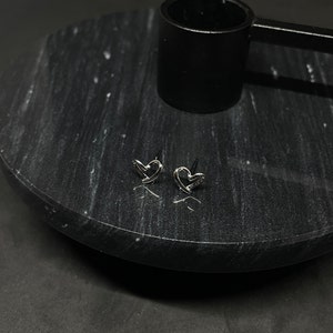 May include: A pair of silver heart-shaped stud earrings on a black marble surface.