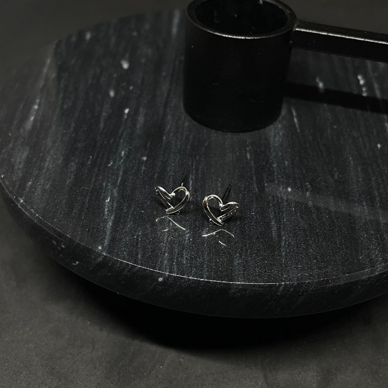 May include: A pair of silver heart-shaped stud earrings on a black marble surface.