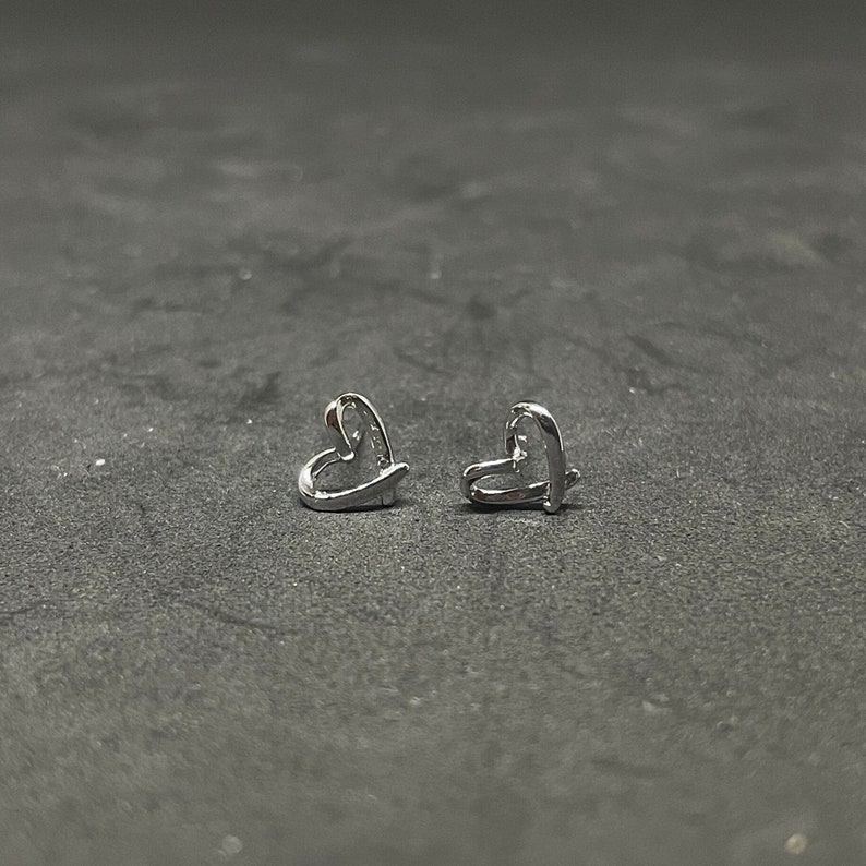 May include: A pair of silver heart-shaped stud earrings. The earrings are simple and delicate, with a smooth, polished finish.