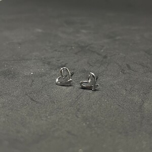 May include: A pair of silver heart-shaped stud earrings.