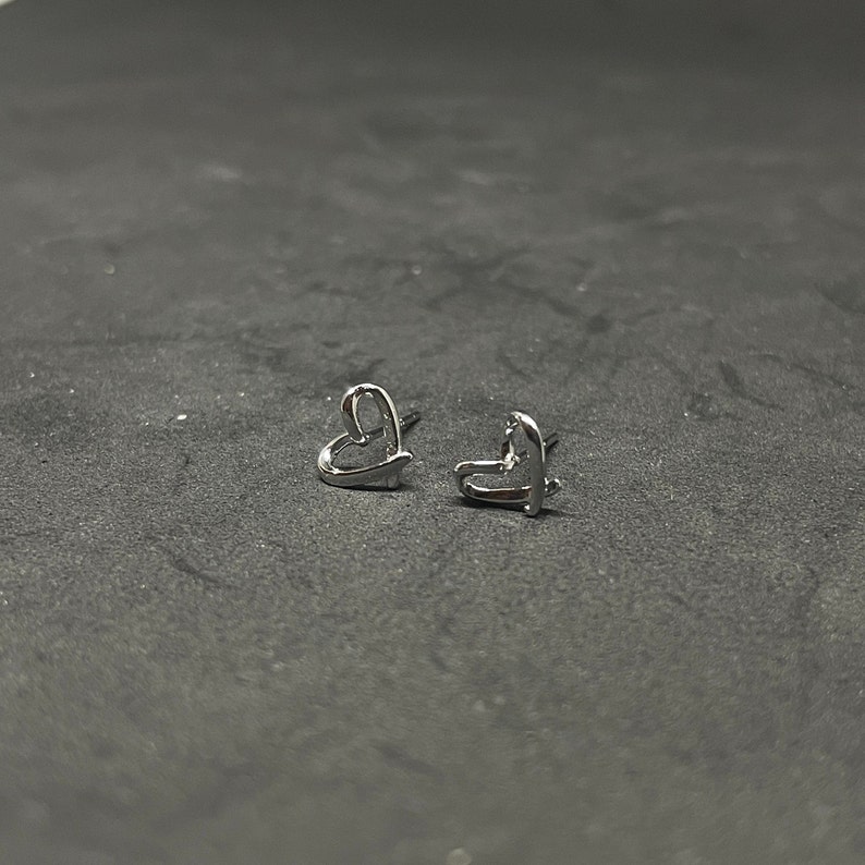 May include: A pair of silver heart-shaped stud earrings.