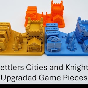 May include: Three sets of upgraded game pieces in orange, yellow, and blue. Each set includes miniature buildings, castles, and other structures. The text "Settlers Cities and Knights Upgraded Game Pieces" is displayed below the game pieces.