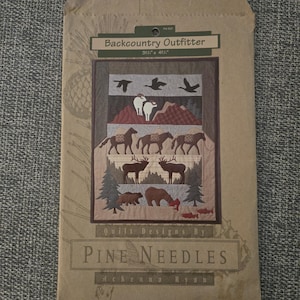 May include: A brown paper envelope containing a quilt pattern titled Backcountry Outfitter by Pine Needles and McKenna Ryan. The pattern features a 31.5 inch by 41.5 inch quilt design with illustrations of birds, mountain goats, horses, elk, bears, and fish.