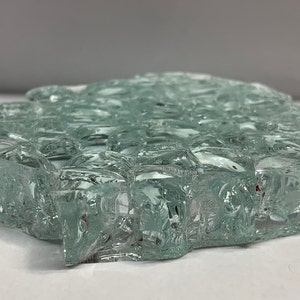 May include: A close-up of a light green, textured glass tile. The tile is made of many small, irregular pieces of glass that have been fused together.