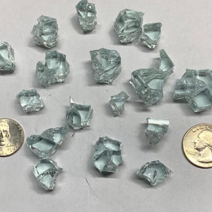 May include: A collection of small, clear glass shards, some with sharp edges, scattered on a white surface. Two US coins are included for scale.
