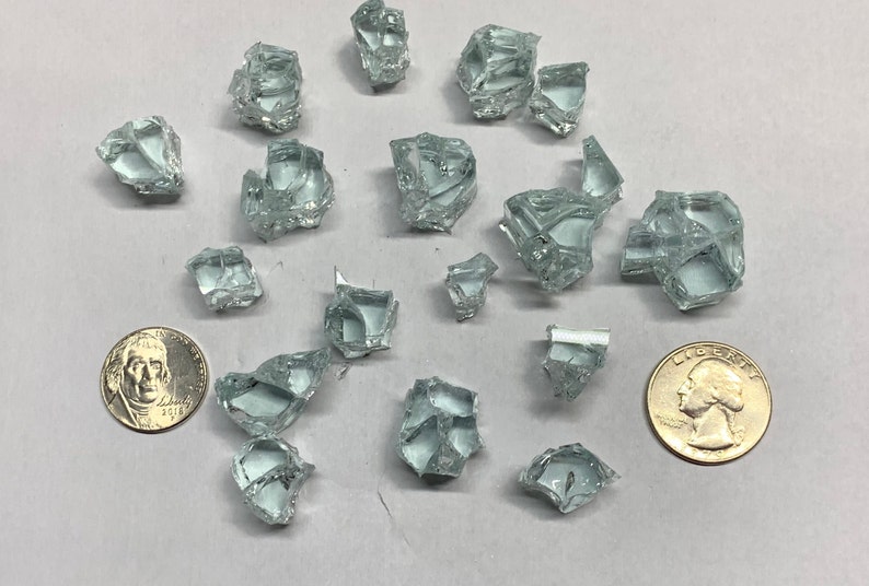 May include: A collection of small, clear glass shards, some with sharp edges, scattered on a white surface. Two US coins are included for scale.