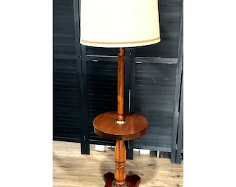 May include: A vintage floor lamp with a cream-colored lampshade and a brown wooden base. The lamp features a small round table and decorative brass accents. The lamp is designed for indoor use and has a classic, traditional style.