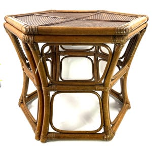May include: A hexagonal bamboo side table with a woven top. The table has a natural brown finish and a geometric design. The legs are curved and connected by rectangular supports. The table is approximately 20 inches wide and 20 inches tall.