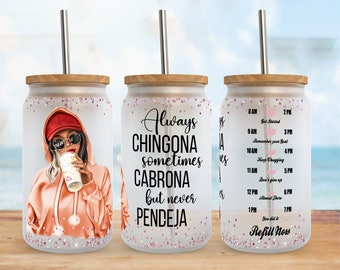 Könnte beinhalten: Ein weißer Becher mit einem rosafarbenen Glitzerdesign und einer Schwarzweißillustration einer Frau, die ein rosa Kapuzenoberteil und eine Baseballkappe trägt. Der Becher hat einen Strohhalm und einen Holzdeckel. Der Text auf dem Becher lautet "Always Chingona sometimes Cabrona but never Pendeja".