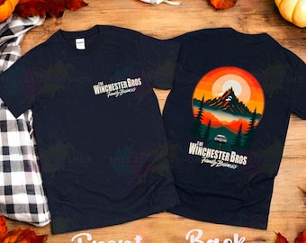 May include: A dark blue t-shirt with a graphic print of a sunset over a mountain range with a car driving on a road. The text "The Winchester Bros Family Business" is printed on the front and back of the shirt.