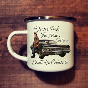 May include: White ceramic mug with a black and white image of a man standing next to a black car. The text on the mug reads "Driver Picks The Music Shotgun Shuts His Cakehole".